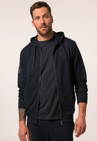 Navy zip-up hoodie with dual side pockets, ribbed cuffs, and a flag detail on the sleeve, paired with a matching t-shirt.