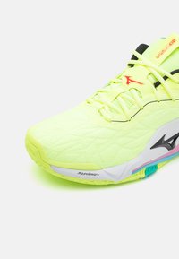 Neon gul atletiksko med en tekstureret overflade, sorte accenter og en multicolor sål. Funktioner inkluderer en snørefront og brandingdetaljer.