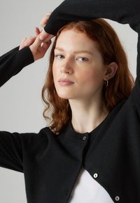 Zwarte cardigan met een ronde halslijn, ribbelmanchetten en subtiele knoopdetails, gemaakt van een zachte, gestructureerde stof.
