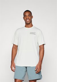 Lys grå kortermet treningsskjorte med rund hals og logo på brystet, sammen med lyseblå shorts med en liten designdetalj.