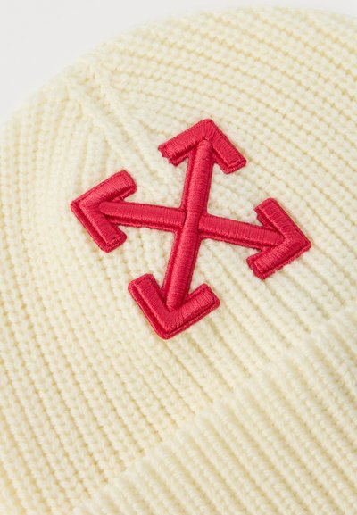 Tissu en tricot crème avec un symbole de flèche à quatre directions brodé en rouge centré sur la surface.