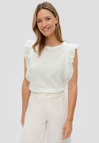 Biała, krótka bluzka z rękawami, z falbankami na ramionach. Gładka tekstura, okrągły dekolt, w połączeniu z jasnymi, wysokimi spodniami.