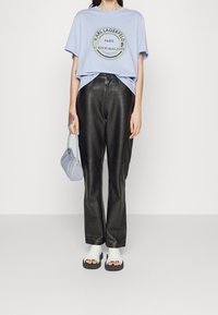 Světle modré tričko s kulatým logem, černé kožené kalhoty, bílo-černé sandály a malá levandulová kabelka.