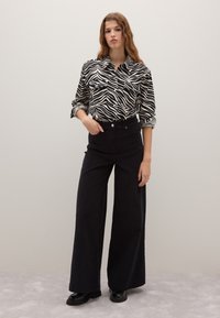 Camisa con estampado de cebra en blanco y negro, con bolsillos abotonados, combinada con pantalones de pierna ancha negros de cintura alta y zapatos de plataforma negros.
