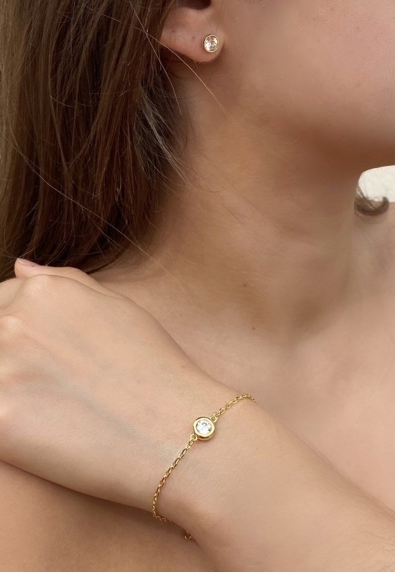 Orecchini e bracciale color oro con design circolari e una pietra trasparente e scintillante al centro. Dettaglio della catena del bracciale visibile.