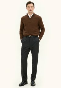 Brauner Strickpullover mit Reißverschluss am Hals, kombiniert mit dunkelgrauen, maßgeschneiderten Hosen und schwarzen Schuhen. Slim-Fit mit glatter Textur.