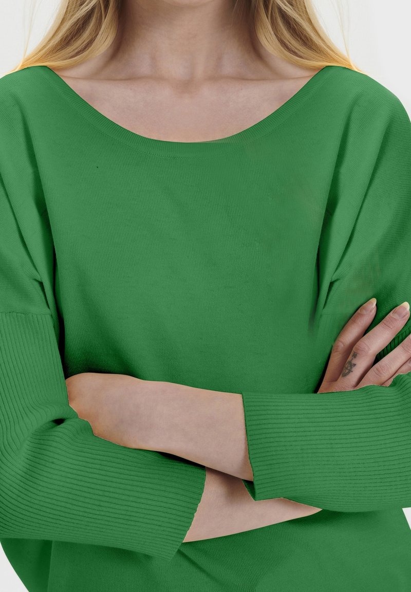 Zielony dziergany sweter o szerokim dekolcie, z prążkowanymi rękawami i luźnym krojem. Tkanina wydaje się miękka i teksturowana.