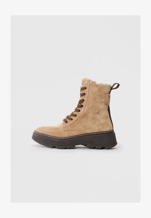 Beige Wildleder Stiefelette mit Schnürung, braunen Schnürsenkeln, weichem Innenfutter, robuster dunkler Sohle und Zuglasche an der Ferse.