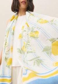 Biały szal z wzorem cytryny i kwiatów, z niebieskimi paskami i żółtymi akcentami. Lekka, miękka tkanina układa się elegancko.