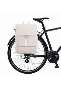 Fehér vászon hátizsák, fedéllel, elülső csatolással és oldalsó zsebbel, egy fekete kerékpárra erősítve, városi használatra.
