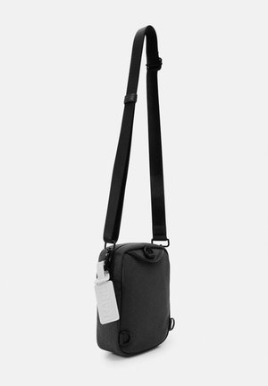 Borsa a tracolla nera in tessuto con tracolla regolabile, forma rettangolare, angoli arrotondati e un'etichetta di marca bianca attaccata sul lato.