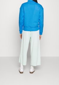 Niebieska bluza z wysokim kołnierzem i prążkowanym dołem zestawiona z jasnoszarymi spodniami o szerokich nogawkach. Model nosi białe sneakersy i skarpetki do kostek.