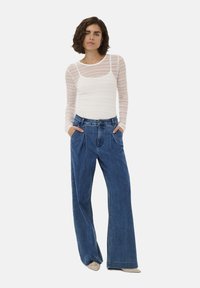 Weißes, langärmliges, strukturiertes Strickoberteil, kombiniert mit blauen, weit geschnittenen Jeans mit hoher Taille und vorderen Falten.