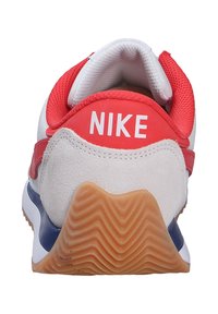 Zapatilla deportiva de Nike con un upper blanco y rojo, talón de malla roja texturizada y suela de goma con patrón en zigzag. Logo en el talón.