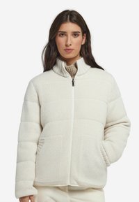 Witte gebreide jas met een hoge kraag, ritssluiting en gestructureerde stof. Voorzien van twee zijzakken en een geribbelde zoom en manchetten.