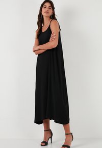 Schwarzes, ärmelloses Maxikleid mit lockerer Passform. Es hat einen Rundhalsausschnitt und reicht bis zum Knöchel, kombiniert mit schwarzen High-Heels.