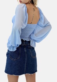 Hellbluse mit Raffung und Puffärmeln, kombiniert mit einem dunkelblauen Jeans-Minirock mit ausgefranstem Saum und zwei Gesäßtaschen.