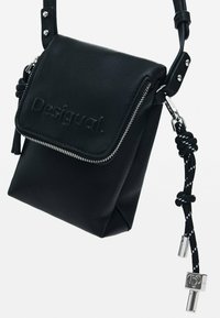 Sac en cuir noir à bandoulière présentant une fermeture éclair, un logo en relief et une surface texturée. Accentué par une bandoulière nouée et du matériel en métal argenté.