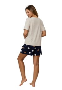 Beżowa bluzka z krótkim rękawem w połączeniu z granatowymi szortami z dużymi białymi i brązowymi kropkami. Gładka tekstura, luźny krój i swobodny design.