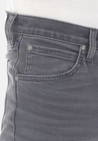 Grijze denim jeans hebben een aansluitend ontwerp met zichtbare stiksels, een voorzak en metalen klinknagels. De textuur is glad met een lichte glans.