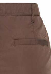 Brown fabric close-up of a back pocket on a pair of trousers with a belt loop and stitched details.