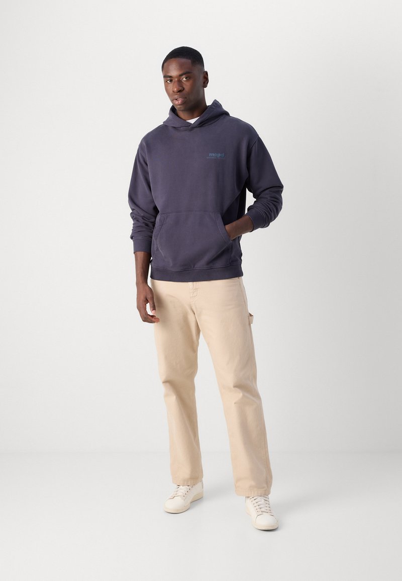 Marineblaues Hoodie mit Kängurutasche, verstellbarem Zugband in der Kapuze und dezendem Logo. Kombiniert mit hellbeigen Hosen und weißen Sneakers.