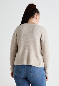 Light beige, ribbed knit sweater with a rounded neckline and long sleeves, paired with blue jeans featuring back pockets and a fitted design.