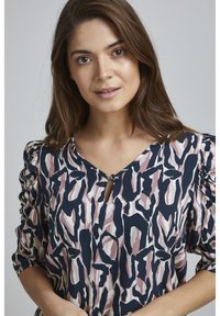 Blusa stampata con base blu navy e motivi astratti in rosa e crema, dettaglio a apertura a chiave sul collo e maniche arricciate per un tocco di texture.
