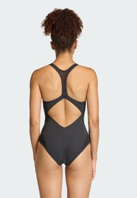 Čierne plavky s dizajnom pretekárskeho chrbta a výrezom na chrbte, s hladkou textúrou a priliehavým tvarom. Vyrobené z elastického, vodoodpudivého materiálu.