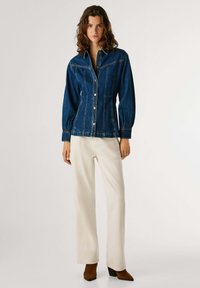 Denimjakke med knappefront, lange puffermer og en lett peplumform. Brukt med kremfargede bukser og brune hælhøyde støvler.