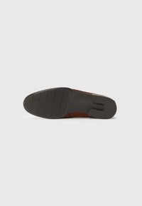 Suela de un zapato de vestir marrón con una suela exterior de goma negra que presenta patrones de agarre y un tacón cuadrado, mostrada sobre un fondo blanco.