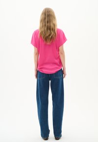 Top rosa brillante a maniche corte con una vestibilità ampia, abbinato a jeans ampi a vita alta blu con tasche posteriori.