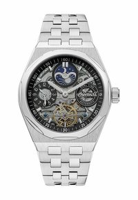 Montre en acier inoxydable avec un cadran squeletté noir présentant des fonctions de double heure, des accents argentés et un tourbillon en ton doré.