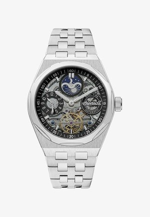Zegarek ze stali nierdzewnej z czarną, szkieletową tarczą, prezentujący funkcje podwójnego czasu, srebrne akcenty oraz złocony tourbillon.