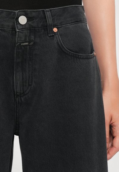 Black denim jeans with copper hardware, featuring a button closure, two front pockets, and a label stitched near the waistband.