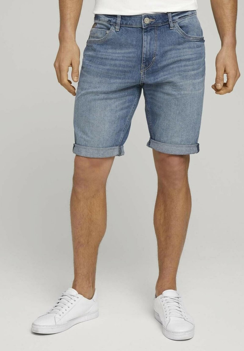 Shorts de mezclilla en azul claro con un diseño clásico de cinco bolsillos, dobladillos enrollados y un cierre de botón de metal, combinados con zapatillas blancas.