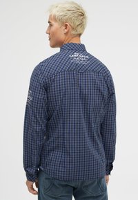 Langärmliges Hemd in blau-schwarzem Karomuster aus leichtem Material mit Knopfmanschetten und gestickten Details auf der Rückseite.