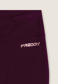 Leggings sportivi viola con una texture liscia, dotati di un logo "FREDDY" in argento in rilievo in vita. Sono visibili le cuciture.