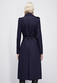 Trench coat della marina con vita aderente, maniche lunghe, spalline e un'apertura sul retro, realizzato in un tessuto liscio e strutturato.