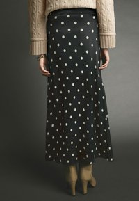 Mustard, täpiline maxi seelik, millel on sile tekstuur, kantud sarnase mustriga kaabliga kudumise siidi singiga ja beežide kandiliste saapadega. Seelik on voolava disainiga.
