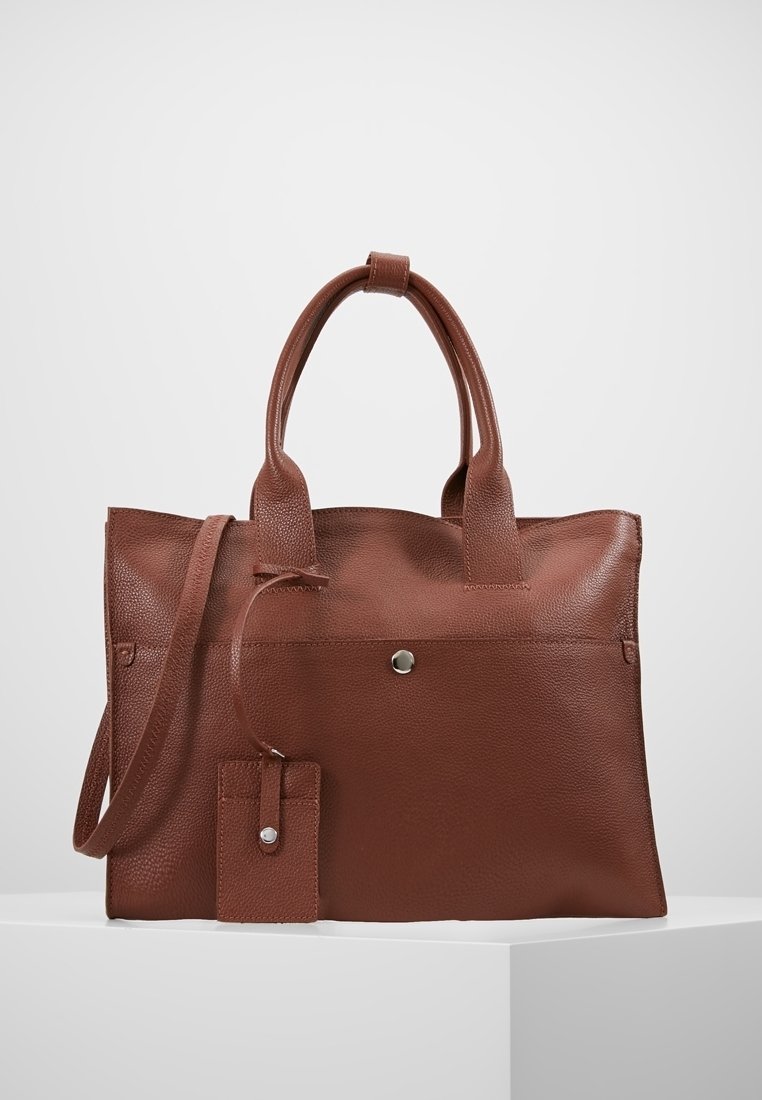 Sac fourre-tout en cuir marron avec doubles poignées, une longue bandoulière et une petite pochette attachée avec un bouton pression.