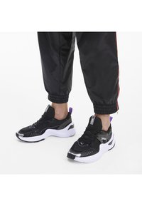 Svart atletiska sneakers med nätmaterial, vit sula, lila accenter och reflekterande detaljer. Designade för komfort och stöd.