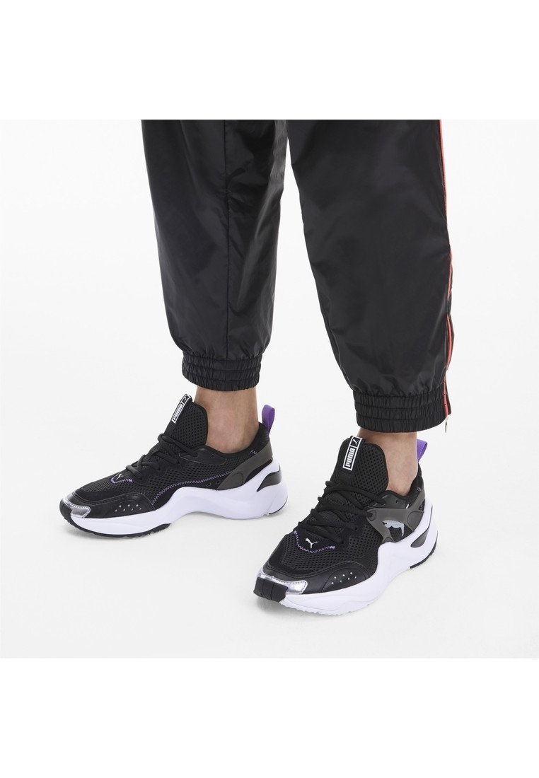 Svart atletiska sneakers med nätmaterial, vit sula, lila accenter och reflekterande detaljer. Designade för komfort och stöd.