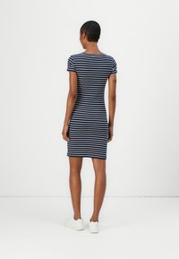 Vestido listrado azul-marinho e branco, com mangas curtas, silhueta ajustada, até ao joelho, feito de um tecido em mistura de algodão, combinado com ténis brancos.