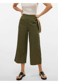 Pantalons larges de couleur vert olive en tissu doux, avec une taille haute et des poches latérales. Associés à des sandales noires à enfiler.