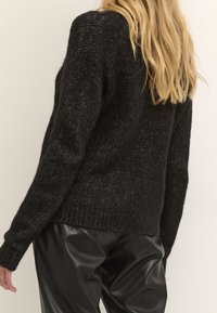 Schwarzer Strickpullover mit lockerer Passform, strukturiertem Stoff, langen Ärmeln und geripptem Saum, kombiniert mit schwarzen Kunstlederhosen.