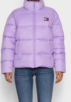 Lavendel pufferjakke med høj krave og lynlås foran, to lynlåslommer, båret med blå jeans, der viser torso og arme.