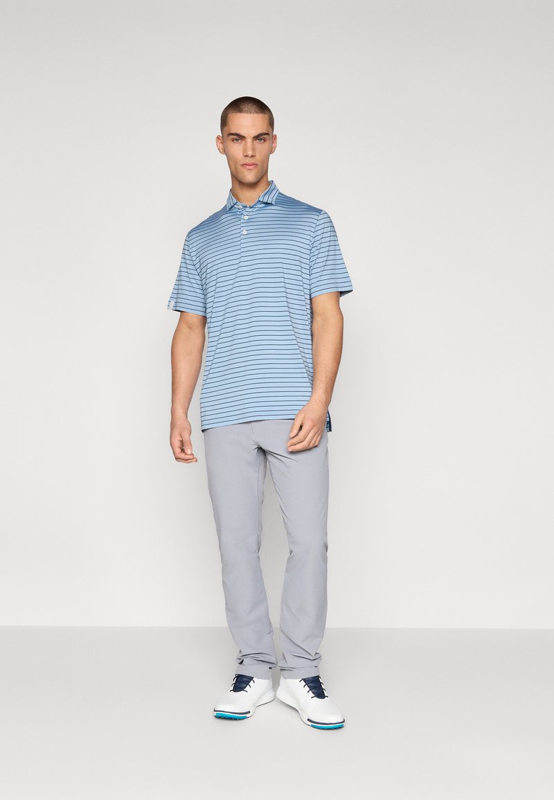 Blårandig polo med krage, bärs med ljusgrå byxor och vita golfskor med blå detaljer. Snygg, avslappnad tyg.