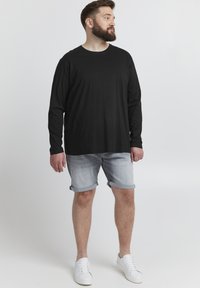 Black long-sleeve shirt paired with light denim shorts, rolled at the hem, and white sneakers. Clean design, casual fit, minimal pattern.