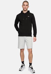 Zwarte hoodie met buidelzak, grijze shorts, zwart-witte sneakers met logo-accenten en contrasterend logo op de hoodie.